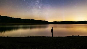 Immagine per l'articolo I tre poteri, raffrigurante una riva di un lago in basso con un uomo che guarda in alto verso il cielo, un lago con delle colline e in alto il cielo stellato