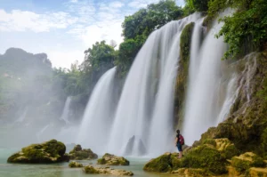 Immagine di una cascata con una ragazza ai piedi della stessa che guarda verso l'alto